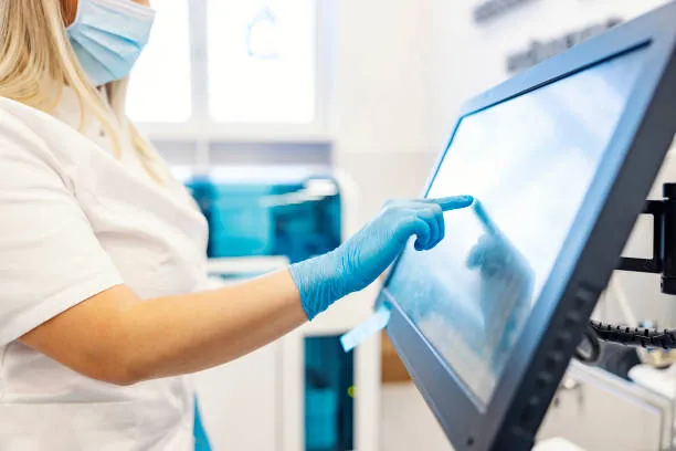 A Nurse Is Standing Next To A Machine For Analyzing Blood Samples And Programing It.