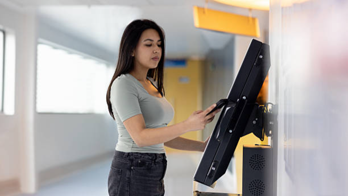 A woman using a tilting touch screen mounted on a wall in a lit corridor