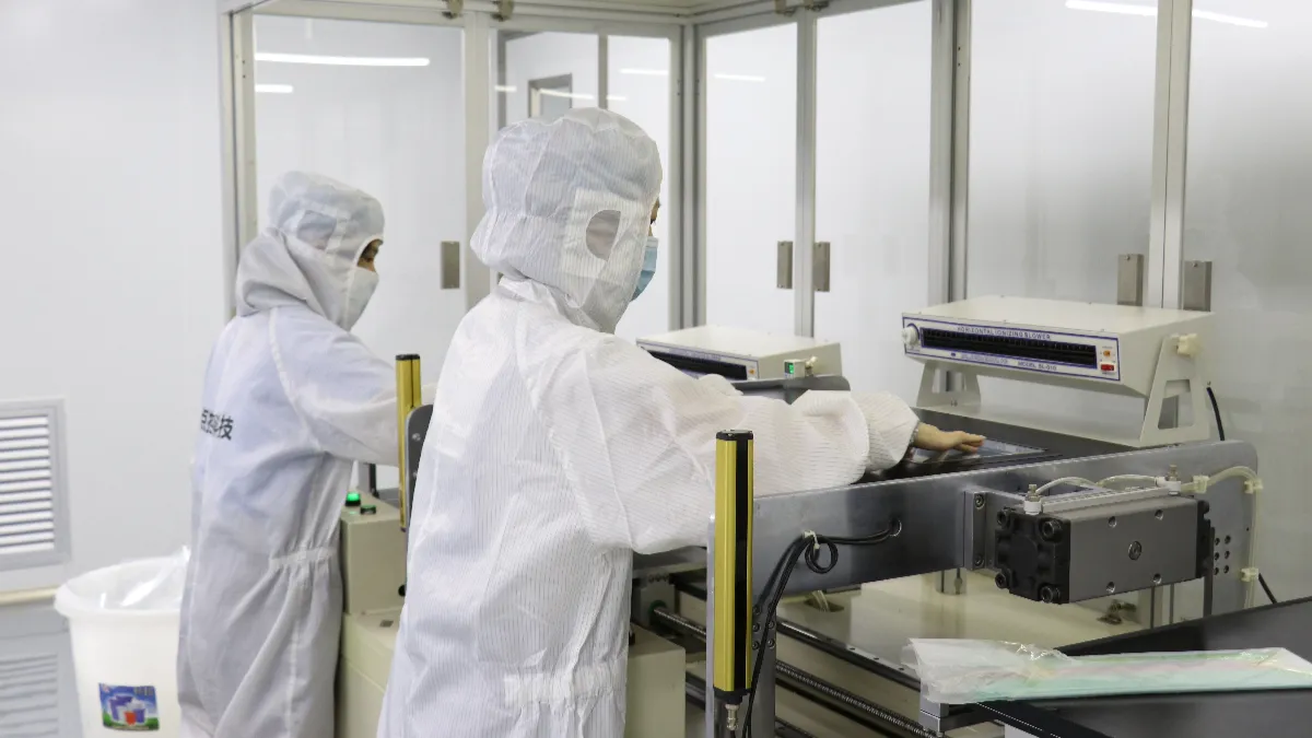 Two workers in cleanroom suits handling touch panels at an inspection station
