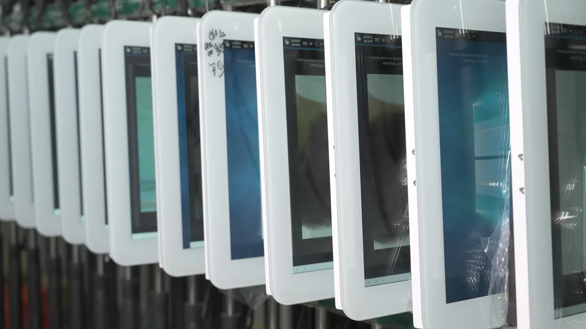 A row of touch displays powered on in a factory burn-in rack