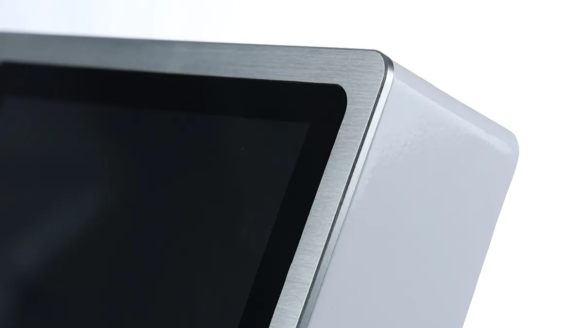 Close view of a brushed metal display bezel meeting a white kiosk enclosure
