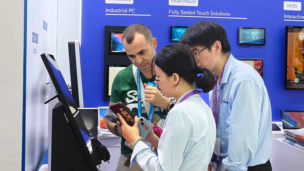 People Examining A Touchscreen Monitor At A Trade Show Booth